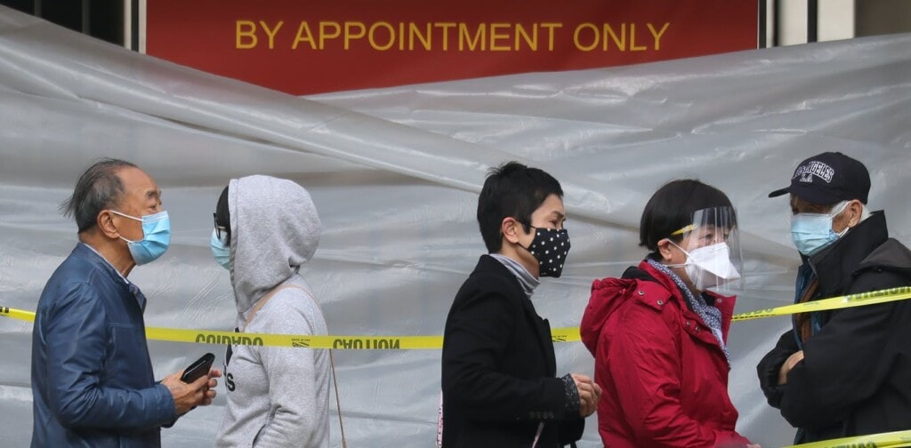 5 people wearing masks waiting in line for a vaccine